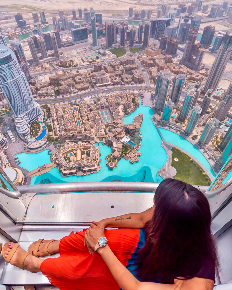 A girl sitting beside glass window at the top of burj khalifa
