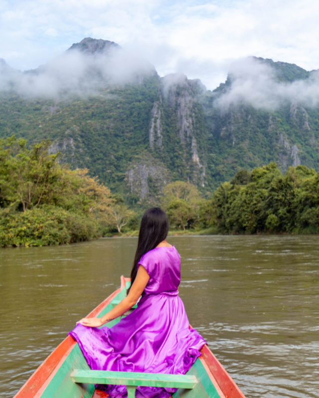 A girl in purple dress siting in a boat with a view of river and mountains