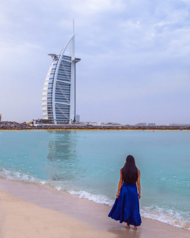 A girl in blue dress at Jumeirah beach with a view of Burj al arab in Dubai