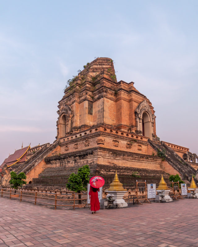A girl in red dress with red umbrella stnding in front of Chedi luang temple