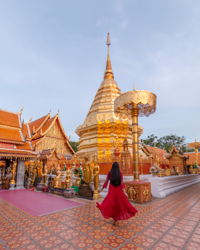 A girl in red dress standing in front of golden cheddi at doi suthep temple