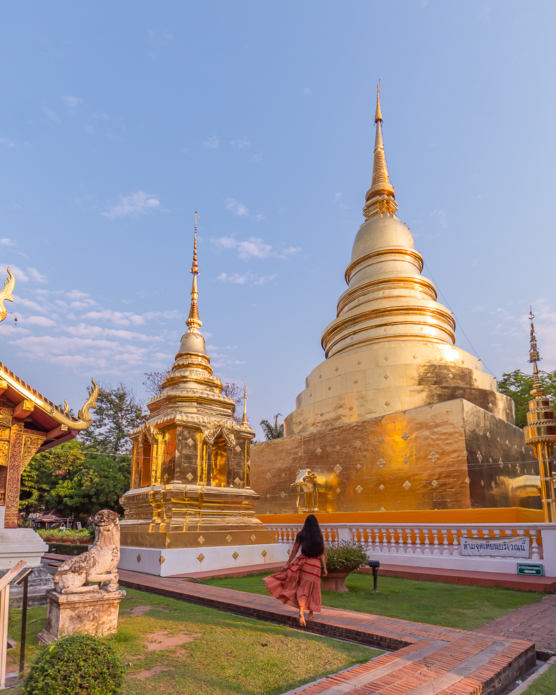 A girl in brown dress standing in front of golden cheddi at wat phra singh