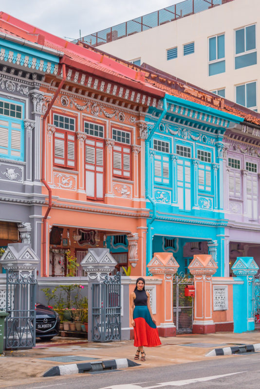A girl in orange skirt posing in front of colorful Peranakan houses in singapore