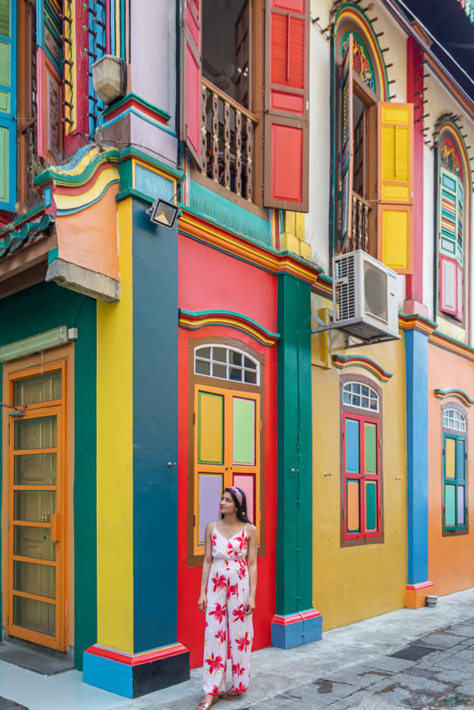 A girl in red jumpsuit standing in front of colorful house at little india in singapore