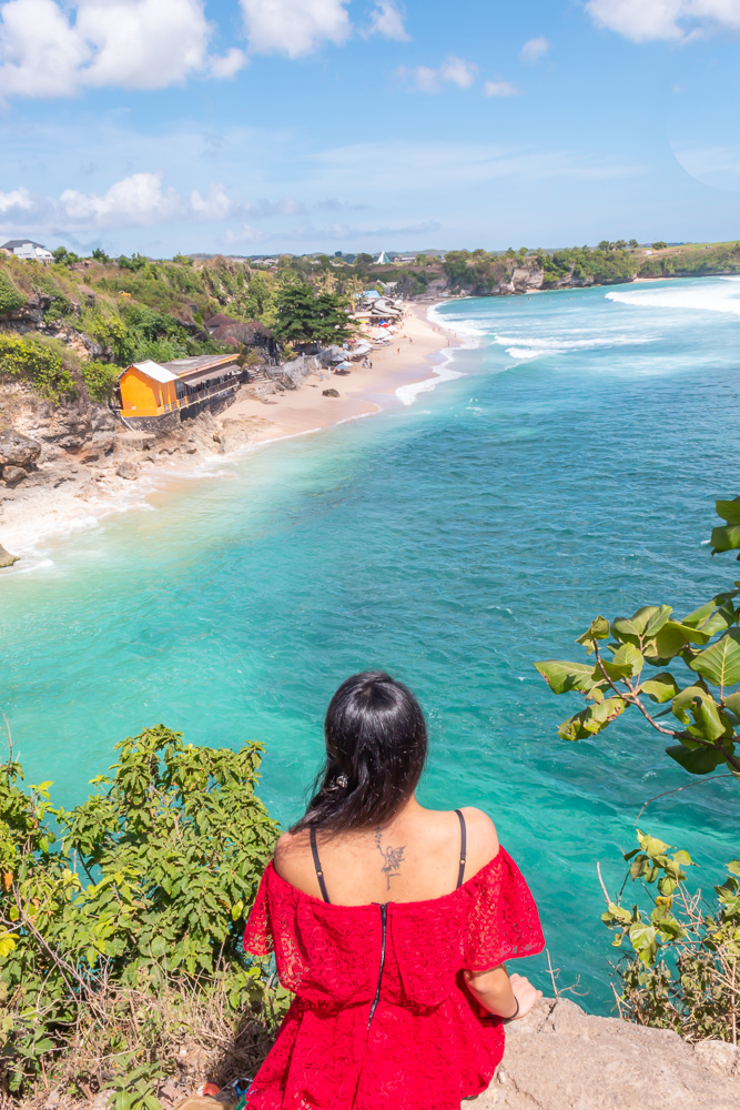 A girl in red dress sitting at the viewpoint of Balangan beach in bali in Indonesia