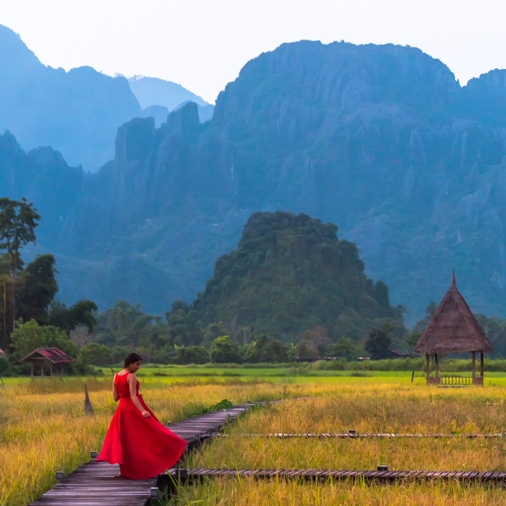 A girl in red dress standing at a pathway surrounded by rice paddies in Vang Vieng, Laos